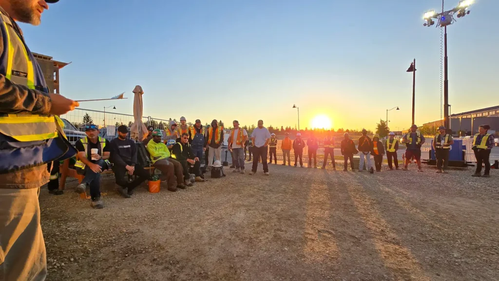 Construction crew gathered on a job site at sunset representing team commitment to continuous improvement